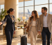 Illustration of an airport host welcoming two travelers with luggage at a premium lounge entrance